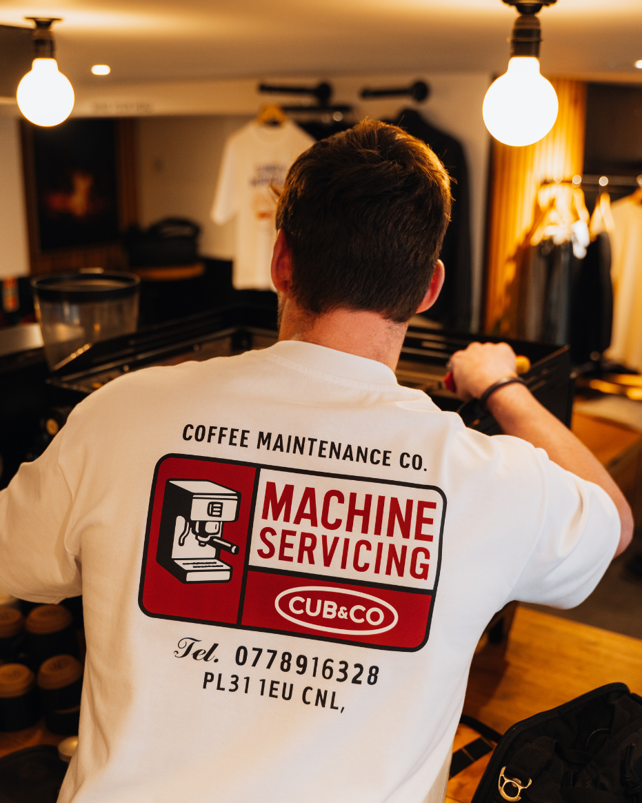 Person wearing a white t-shirt with a coffee shop-themed design in a kitchen setting.
