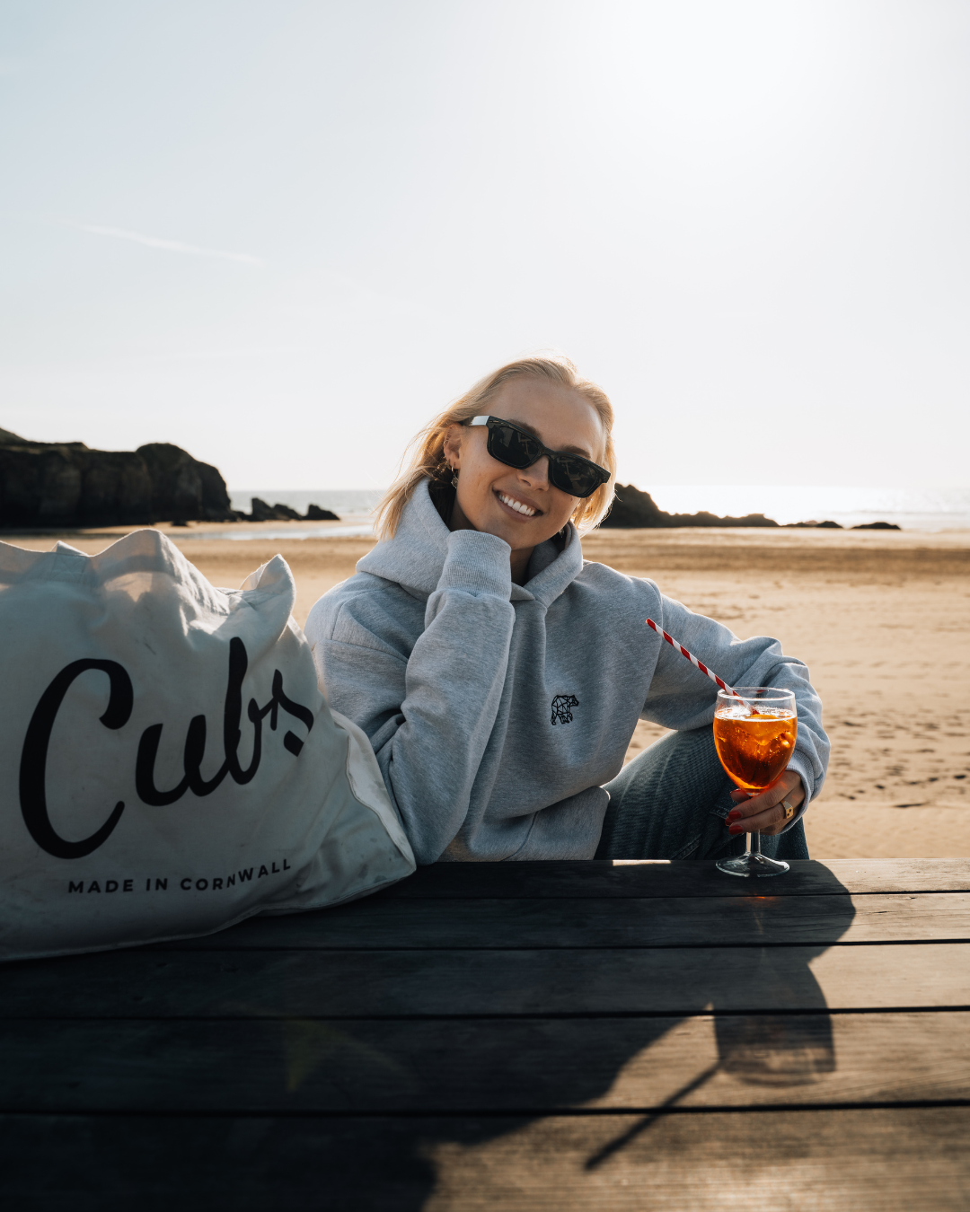 Person sitting on a beach with a drink and a bag labeled &