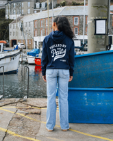 Person wearing a hoodie with text by a waterfront with boats and buildings.