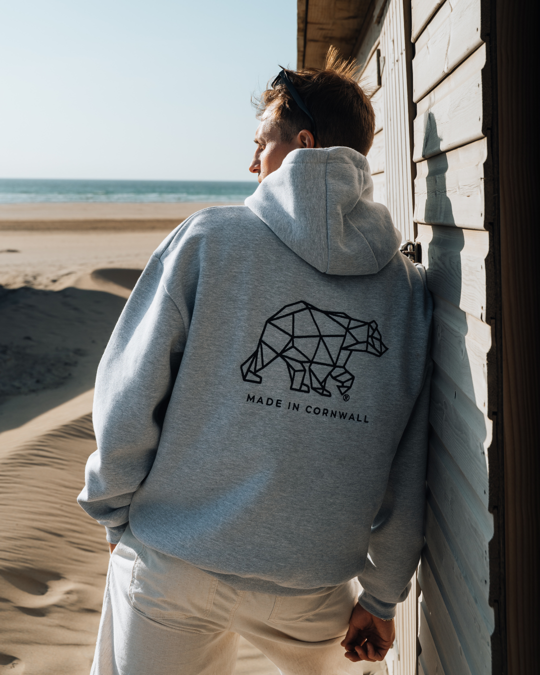 Person wearing a gray hoodie with a geometric bear design on the beach.